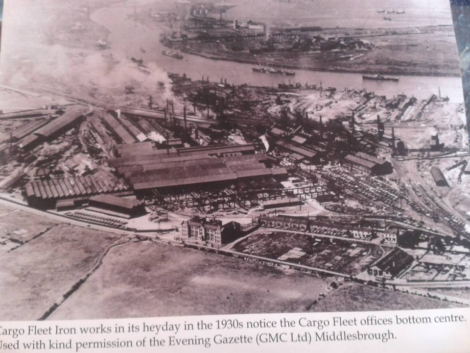 "Cargo Fleet Iron Works in its heyday in the 1930s." Offices in foreground. Row of houses to the right of, and behin the offices. River behind steelworks.